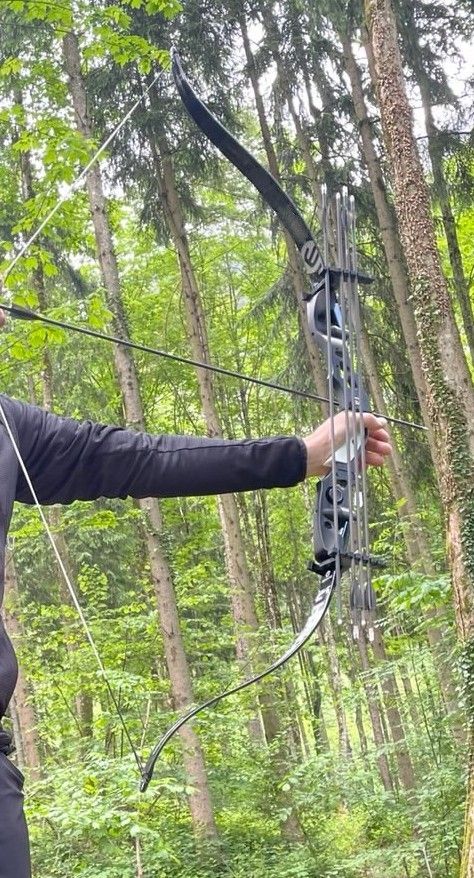 A person wearing a black outfit drawing a bow in a forested area with trees in the background useing the q7-system limb quiver